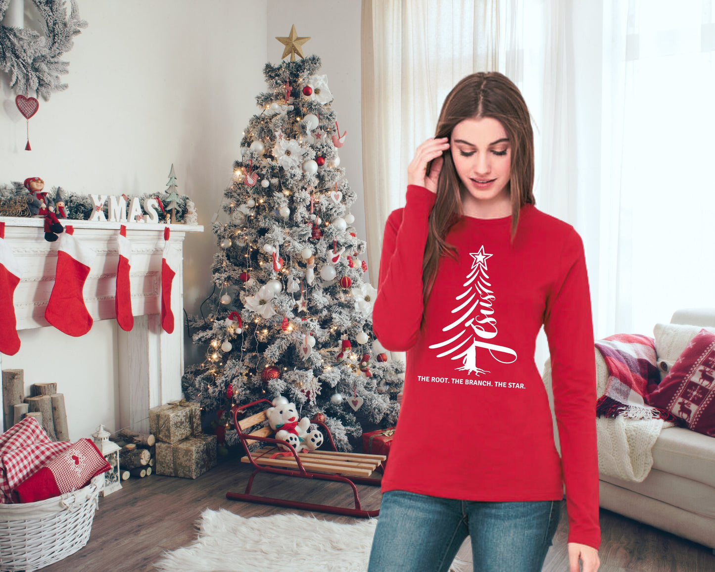Woman in red long-sleeve tee in front of a Christmas tree. Shirt has a white design of a tree incorporating the word Jesus.