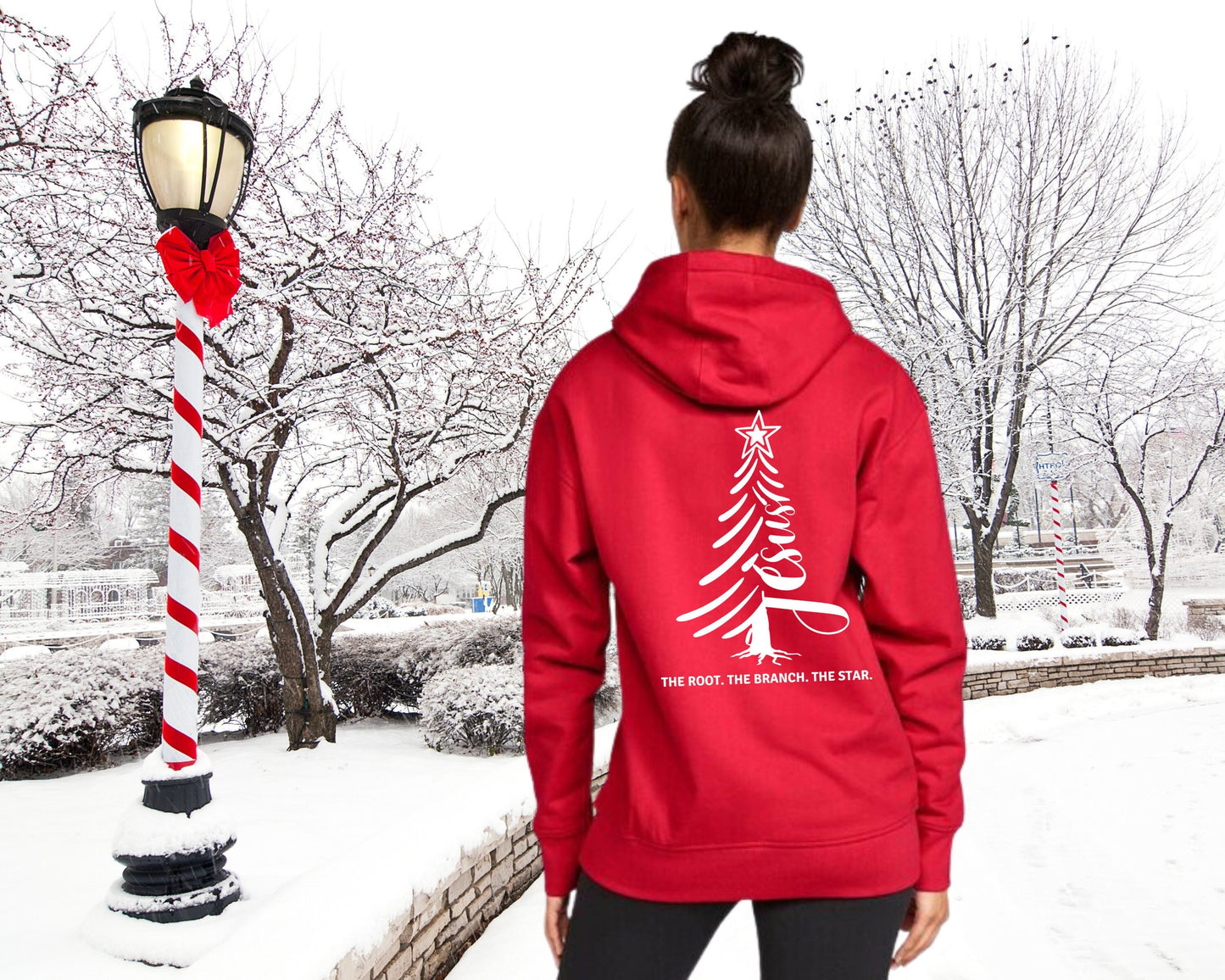 Woman standing in a snowy scene with a red hoodie on. The back of the hoodie has a design of a Christmas tree with the word Jesus incorporated into it.