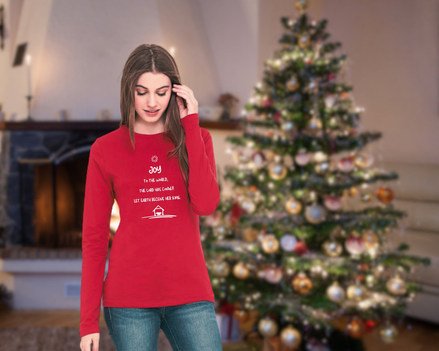 Woman standing in front of a Christmas tree wearing a red long sleeve tee with the words of Joy to the World on the front in the shape of a tree.