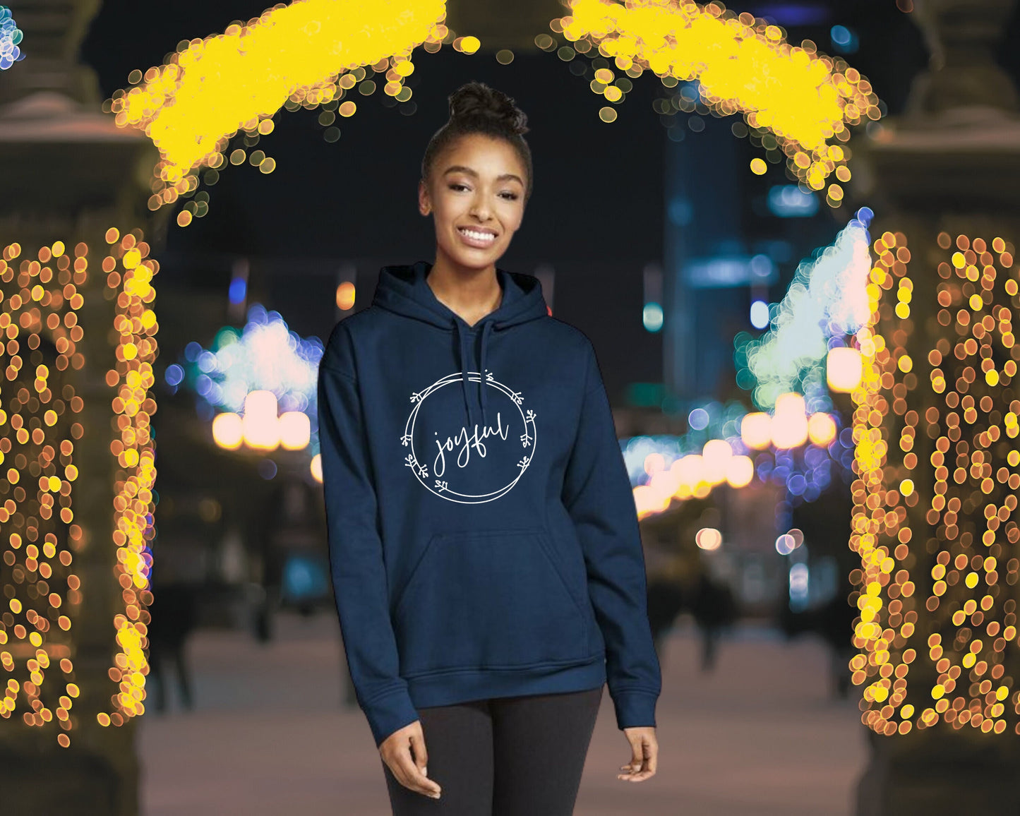 Woman in a navy blue hoodie with a holiday wreath surrounding the word "joyful"