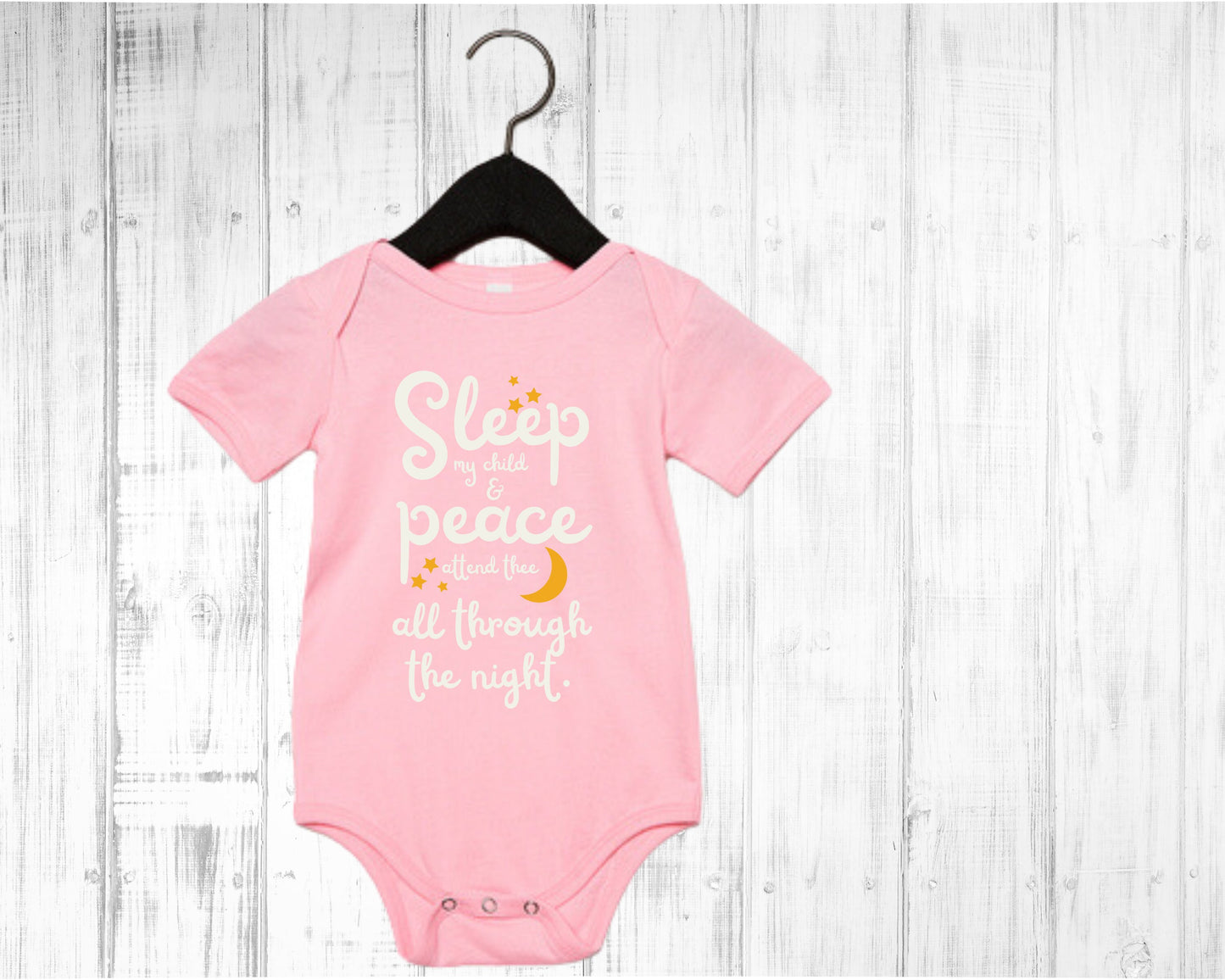 Pink baby onesie with white lettering with the words from the lullaby, "Sleep my child and peace attend thee all through the night." Stars and moon in gold.
