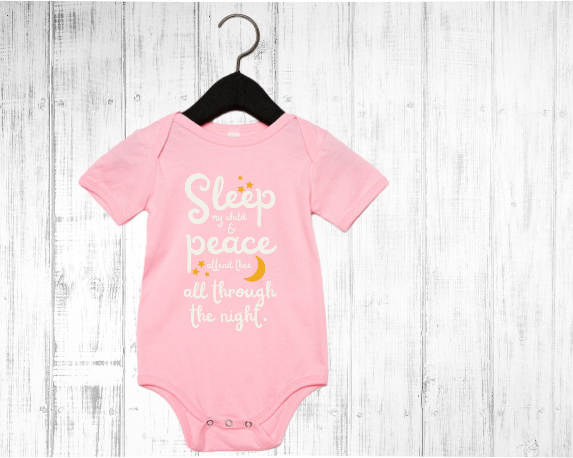 Pink baby onesie with white lettering with the words from the lullaby, "Sleep my child and peace attend thee all through the night." Stars and moon in gold.