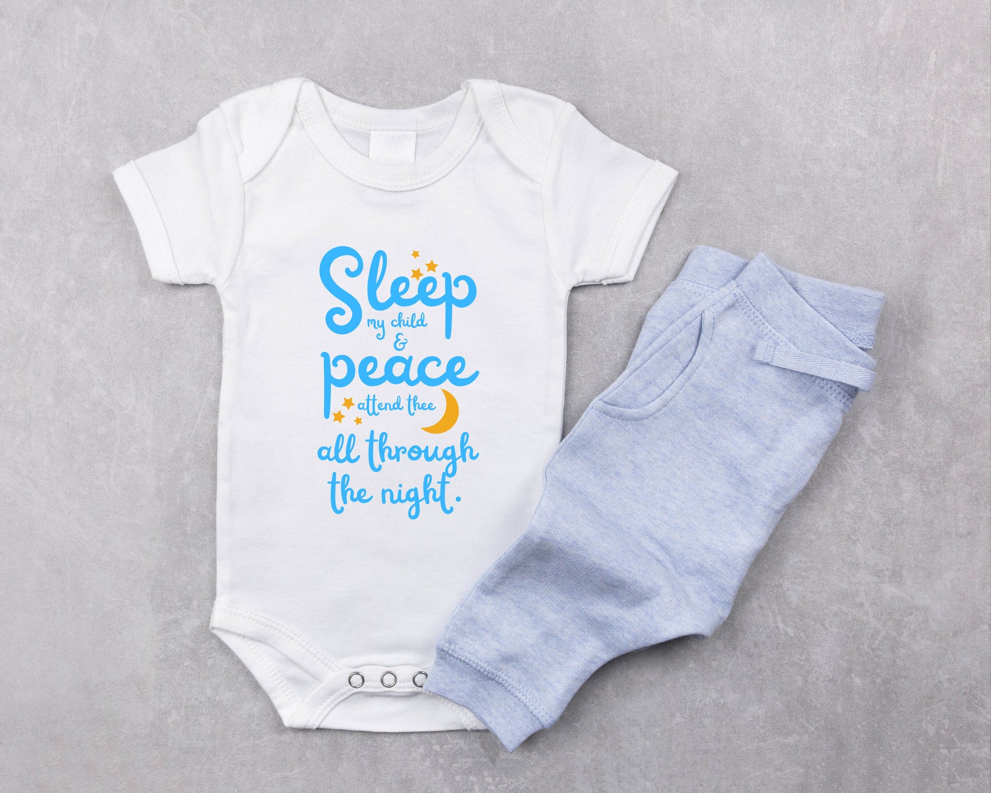 White baby onesie with blue lettering with the words from the lullaby, "Sleep my child and peace attend thee all through the night." Stars and moon in gold.