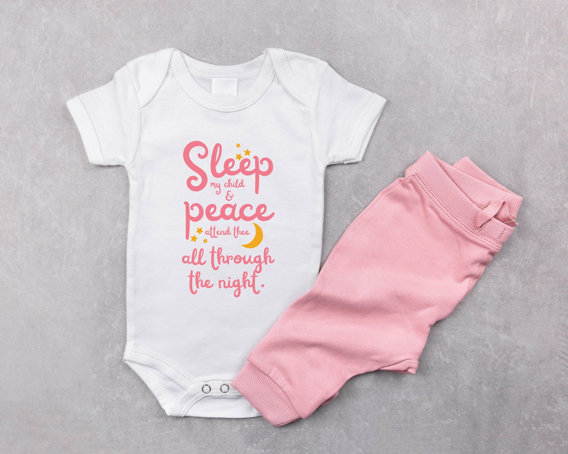 White baby onesie with pink lettering with the words from the lullaby, "Sleep my child and peace attend thee all through the night." Stars and moon in gold.